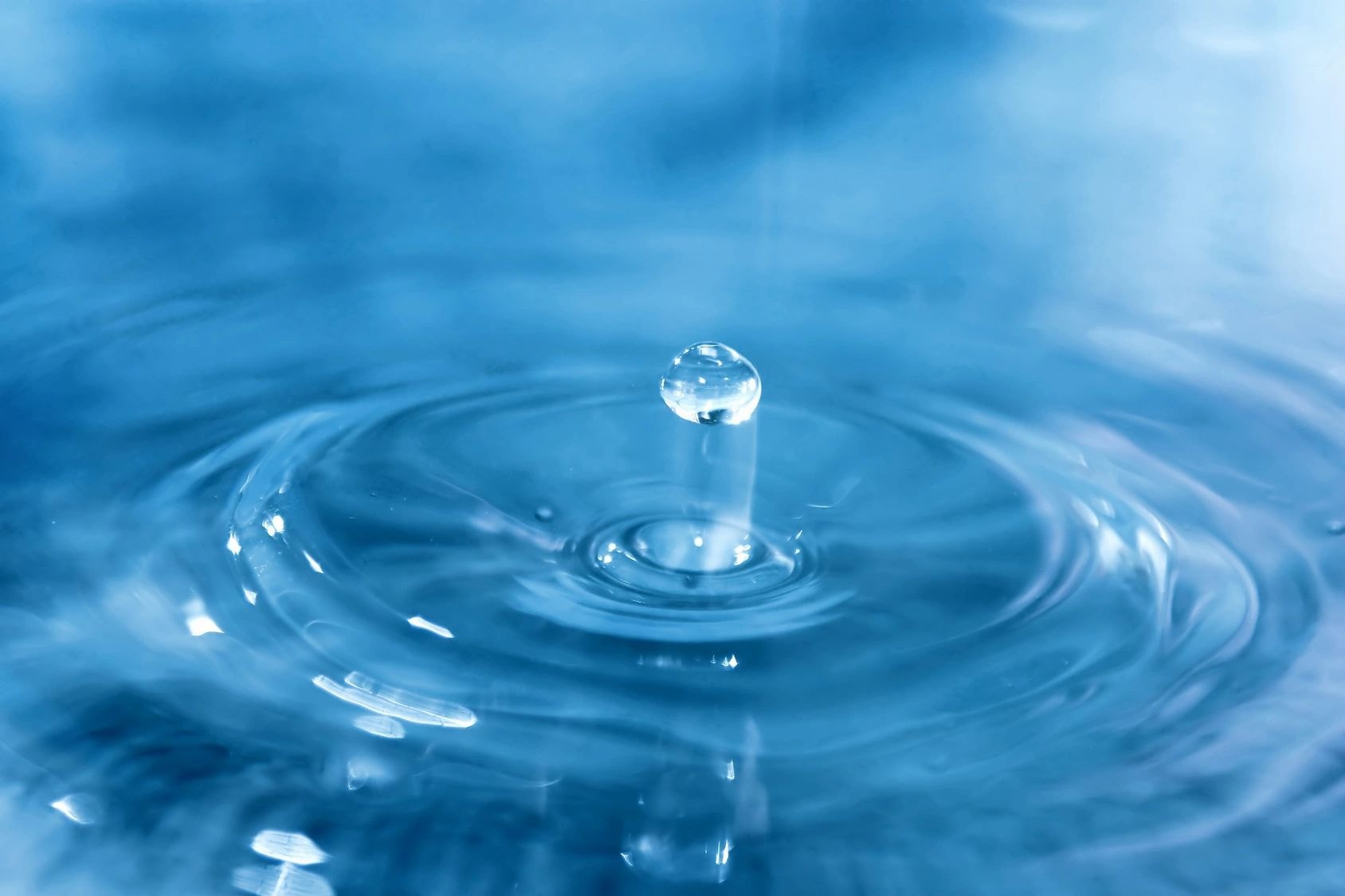 Water droplet creating ripples blue surface